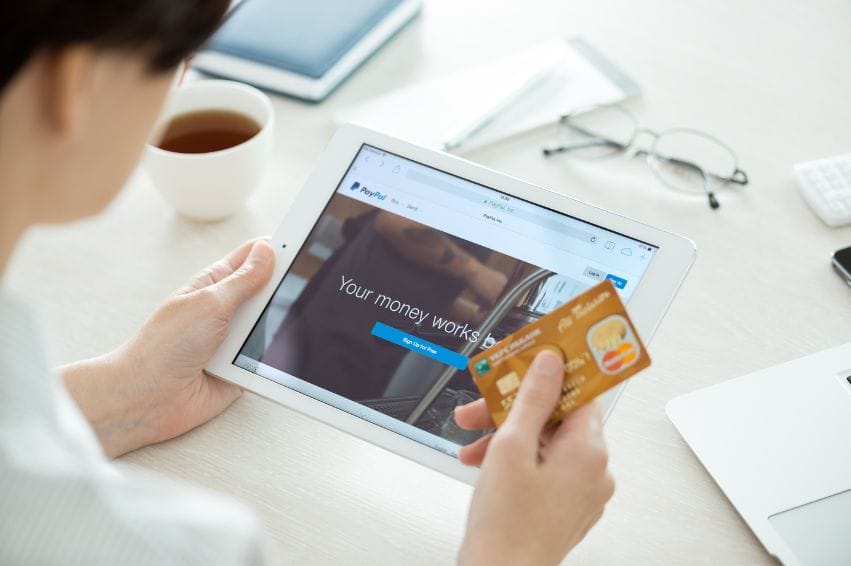 Person with credit card in hand looking on a brand new Apple iPad Air with Paypal website on a screen